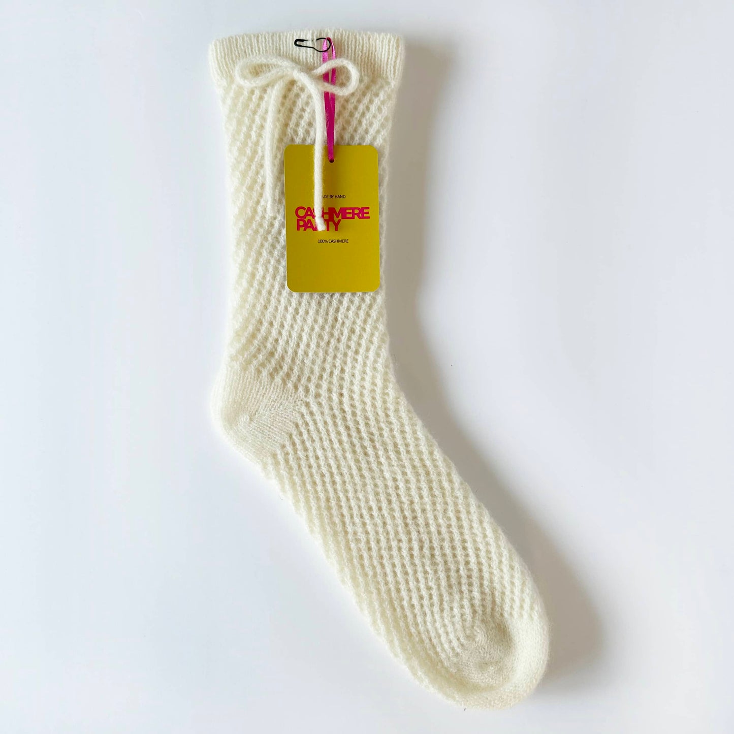 Flat image of pure cashmere handmade sock.  Knitted lace mesh sock with bow detail on ankle by Cashmere Party with branded swing ticket.