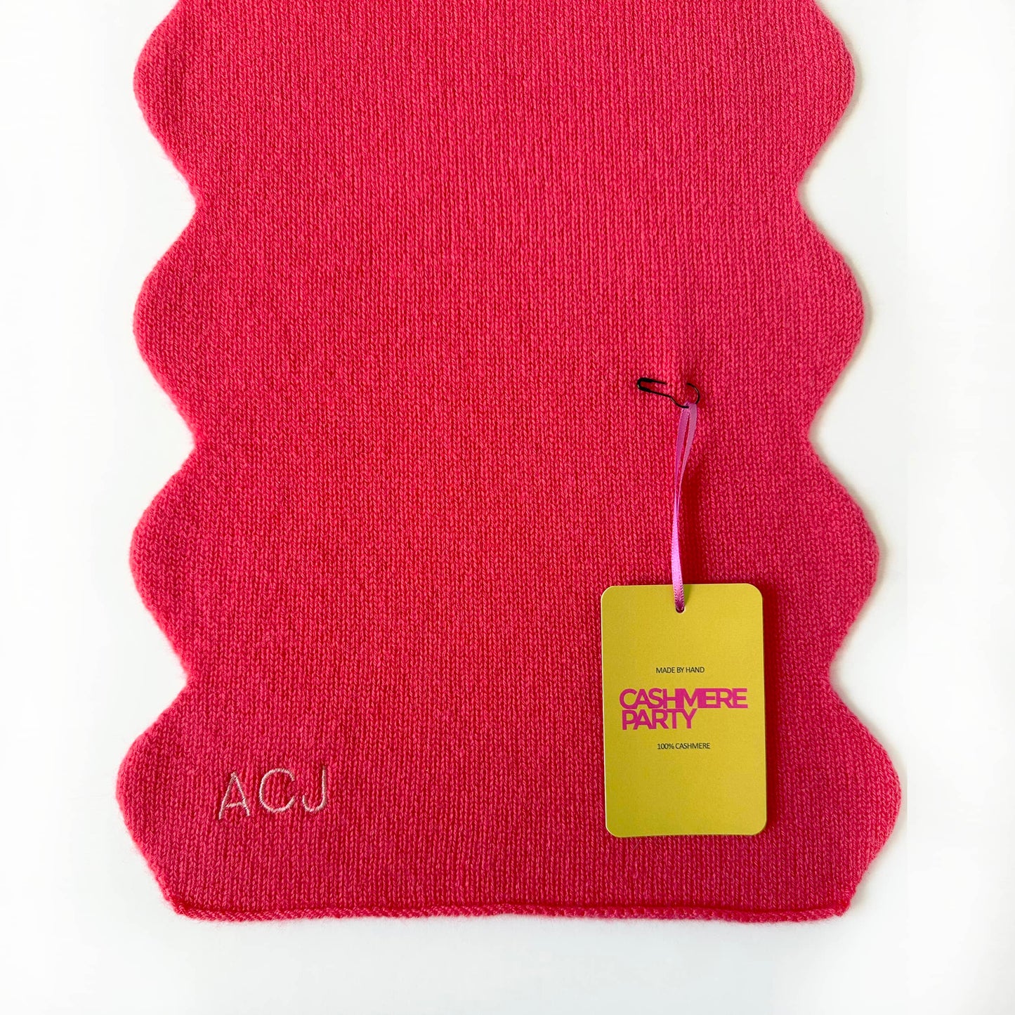 Pure cashmere scarf in red colour with wavy scallop edge and personalisation.  Laying flat on a table with branded Cashmere Party swing ticket.