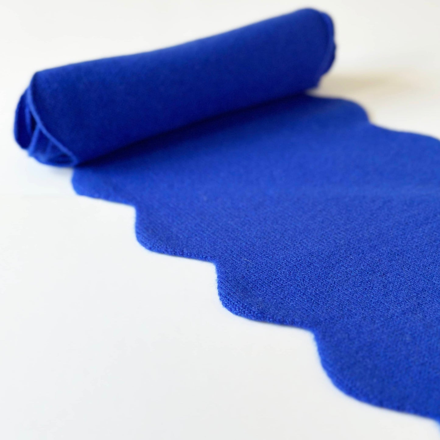 Pure cashmere scarf in bright blue with scallop edges on table.