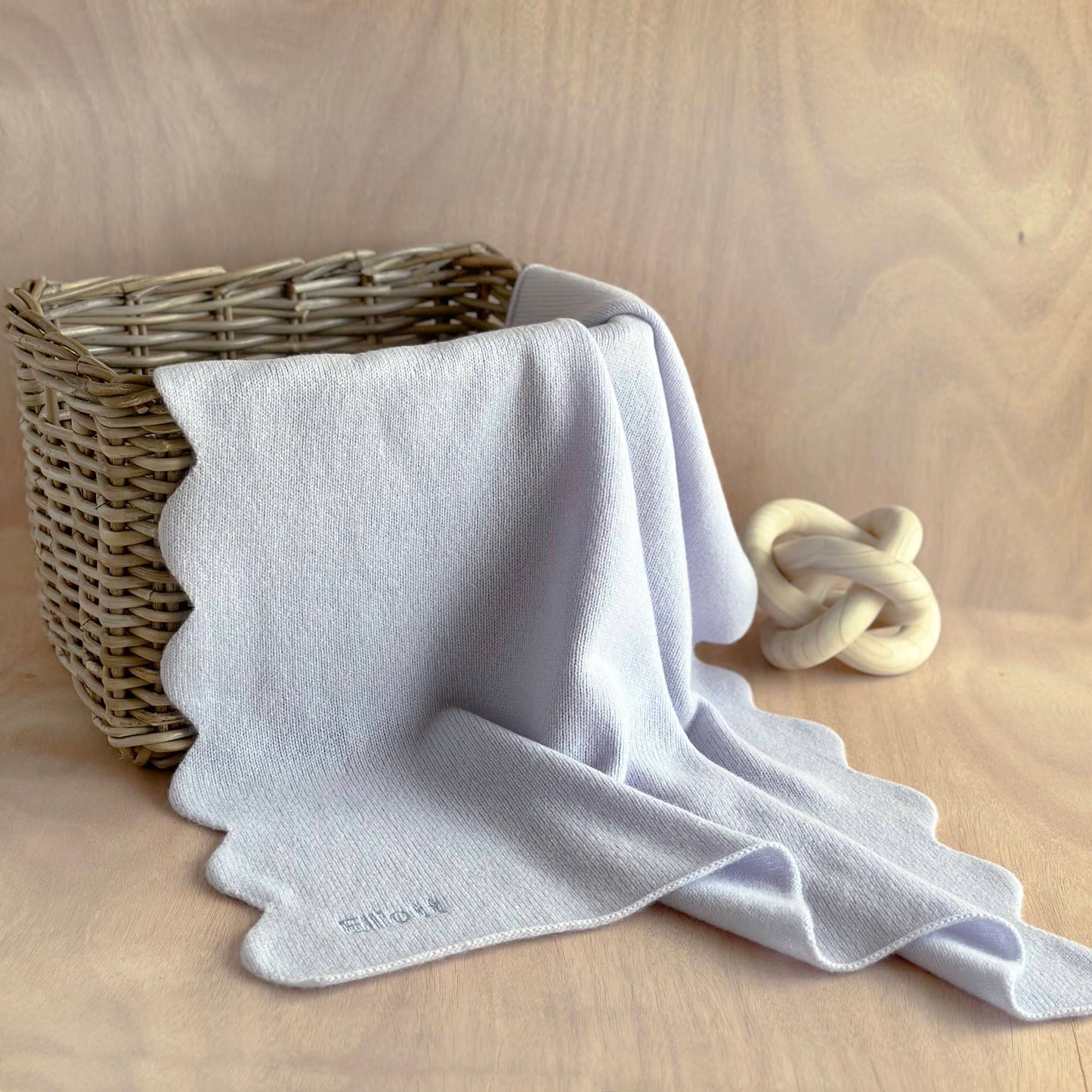 Scalloped edge baby blanket in light blue cashmere on table draped over a wicker basket 